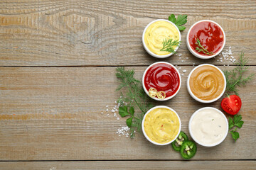 Different sauces and herbs on wooden table, flat lay. Space for text