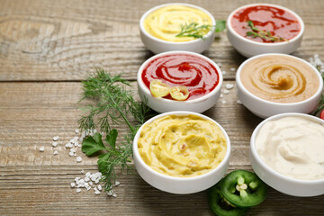 Different sauces and herbs on wooden table, closeup. Space for text