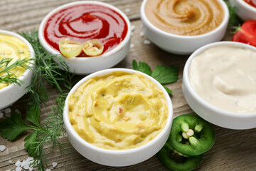 Different sauces and herbs on wooden table, closeup