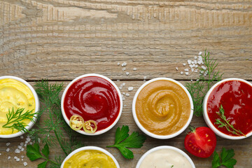 Different sauces and herbs on wooden table, flat lay. Space for text