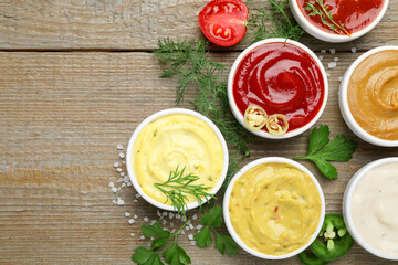 Different sauces and herbs on wooden table, flat lay. Space for text