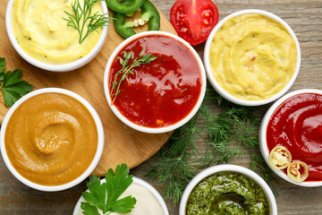 Different sauces and herbs on wooden table, flat lay
