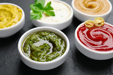 Different sauces and parsley on black table, closeup