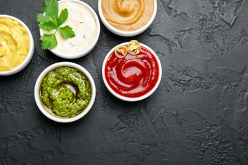 Different sauces and parsley on black table, flat lay. Space for text