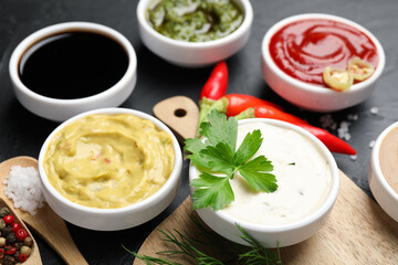 Different sauces, spices and herbs on black table, closeup