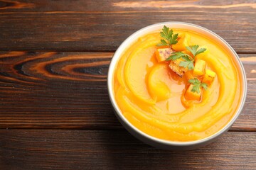 Delicious pumpkin cream soup with parsley served on wooden table, closeup. Space for text