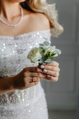 A close-up of the bride, without her face, holding a boutonniere