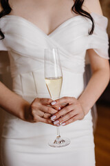 A close-up of a bride, without a face, holding a glass of champagne