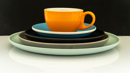 Close up of a colorful porcelain cup of coffee, saucer and plates, on a black background. Hotizontal image.