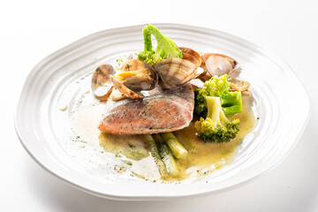 Grilled salmon fillet with clams, asparagus spears, and broccoli florets on a white plate, served with a creamy yellow sauce. A delicious and healthy seafood dinner.