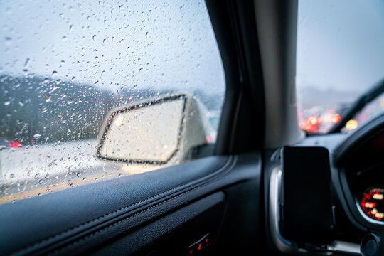 looking out a car window into light reflecting in the side mirror while it's raining