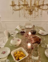 Elegant Holiday Dinner Table with Candles and Roast Meal; a roast meal, golden potatoes, fine china with floral details, crystal glassware, and glowing candles beneath a luxurious chandelier