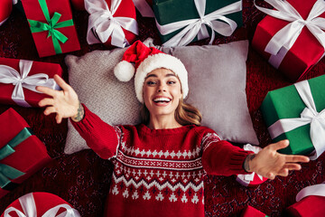 funny festive moment a woman in christmas sweater smiling with gifts around a cozy christmas room...