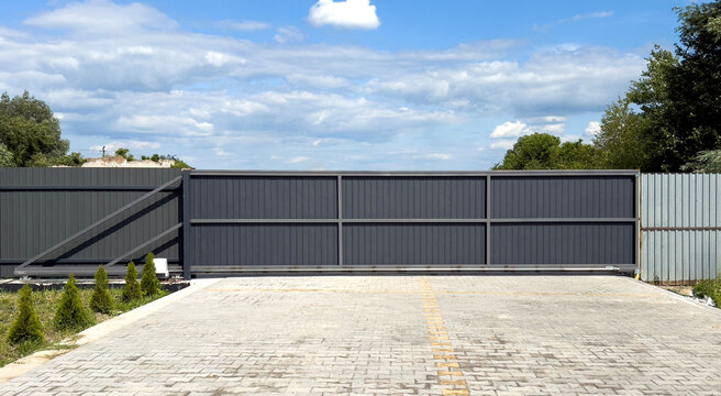 Dark gray metal sliding gate on paved driveway