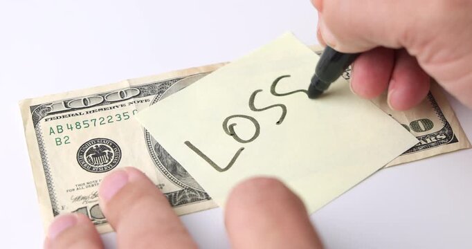 Hand writing the word LOSS on yellow post it beside 100 dollar bill on white background, concept of money setback and financial risk