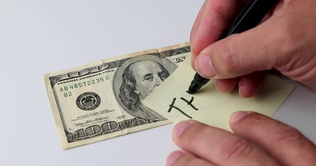 Hand writing the word THANKS on yellow post it beside 100 dollar bill on white background, concept of gratitude, appreciation and reward