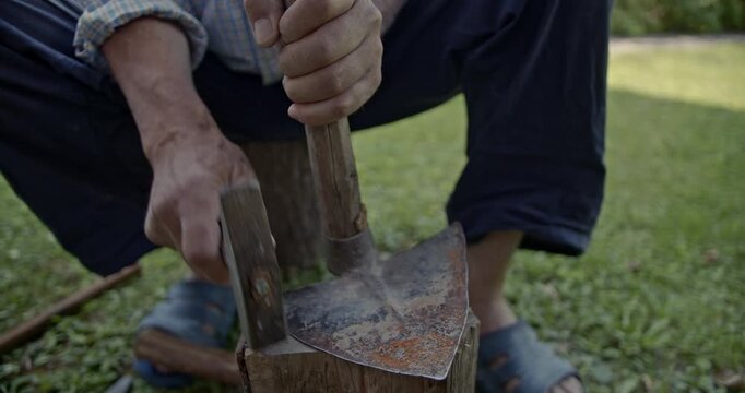 Experience the authentic sounds of a man meticulously sharpening an old, rusty axe with a hammer and wood block outdoors. This manual process highlights traditional craftsmanship.