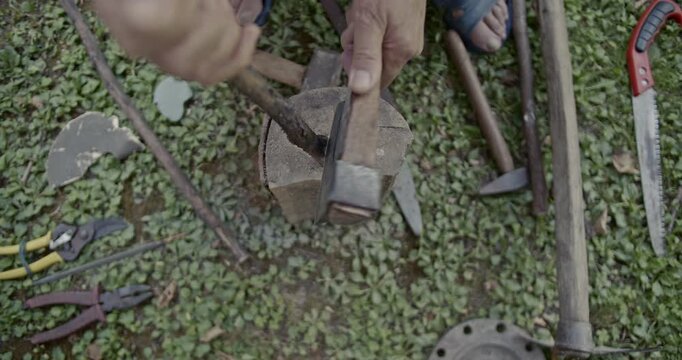 Close-up view of hands meticulously splitting a log with a hammer and chisel on a grassy surface, complemented by the clear sounds of impact and wood breaking. Various hand tools are scattered around.