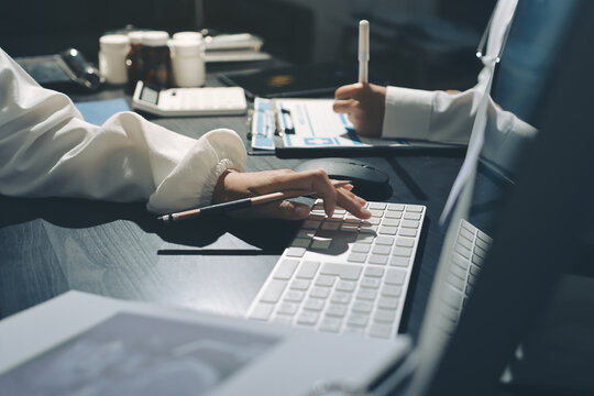 Two doctors and a female nurse meet at a table in the hospital, collaborating on medical tasks using laptops and computers