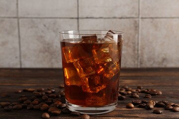 Tasty coffee with ice in glass and beans on wooden table against tiled wall, closeup