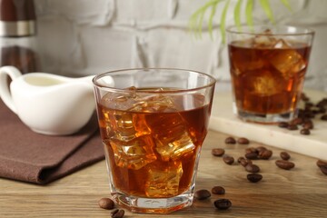 Tasty coffee with ice in glasses and beans on wooden table against light textured background, closeup