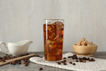 Tasty coffee with ice in glass, beans and sugar cubes on wooden table against grey background, closeup