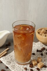 Tasty iced coffee with milk in glass, beans and sugar cubes on wooden table against grey background, closeup