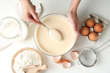 Woman making batter (liquid dough) at white table, top view