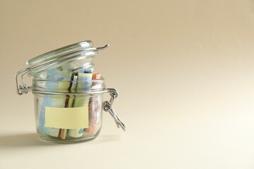 Saving money. Jar with banknotes on beige background, space for text