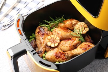 Air fryer with grilled chicken drumsticks, spices and green peas on grey table, closeup
