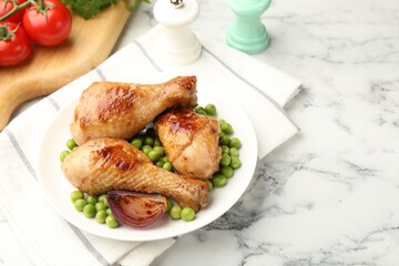 Grilled chicken drumsticks served with green peas on white marble table, above view. Space for text