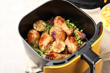 Air fryer basket with grilled chicken drumsticks, spices and green peas on grey table, closeup