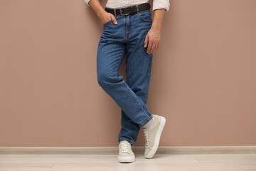 Man in stylish jeans near beige wall, closeup