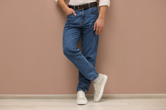 Man in stylish jeans near beige wall, closeup