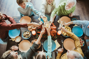 Family Thanksgiving gathering around a long table to celebrate with friends and relatives toasting with glasses and sharing turkey and feast during a warm holiday dinner