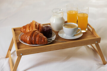 Tray with delicious breakfast on bed in hotel room, closeup