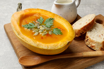 Tasty pumpkin cream soup with seeds, parsley and bread on grey textured table, closeup