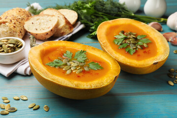 Tasty pumpkin cream soup with seeds and parsley on light blue wooden table, closeup