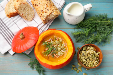 Tasty pumpkin cream soup with seeds, bread and dill on light blue wooden table, flat lay