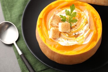 Tasty pumpkin cream soup with croutons and parsley served in pumpkin on grey table, closeup