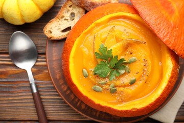 Tasty pumpkin cream soup with seeds and parsley served in pumpkin on wooden table, flat lay