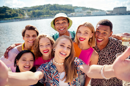 Group of cheerful young friends enjoying a sunny day by the water, celebrating their vacation with laughter and bonding