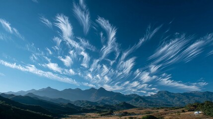 Stunning wispy clouds paint a dramatic sky above layered mountain peaks and arid valley landscape under brilliant blue