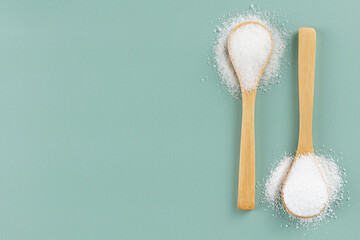 Stevia powder, white sugar in wooden spoons on a green background. Natural and artificial sweeteners. Copy space