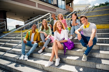 Obraz premium Diverse group of cheerful young friends sitting on stairs enjoying a sunny day in the city, bonding in vibrant styles