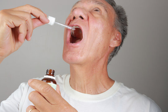 Older Man applying medical prescription drops in his mouth for pain relief