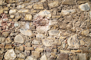A wall made of natural stones of irregular shape and gray brown color on a clear sunny day. The design of the backgrounds structure.