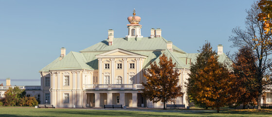 Grand Menshikov Palace in Oranienbaum ensemble surrounded by autumn trees under clear blue sky on a sunny day.