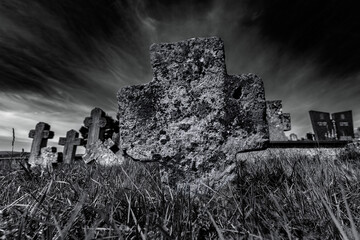 Black and white image of an ancient stone cross under moody clouds, evoking themes of faith,...