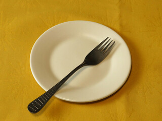 Close-up of a fork on a white plate on a yellow tablecloth